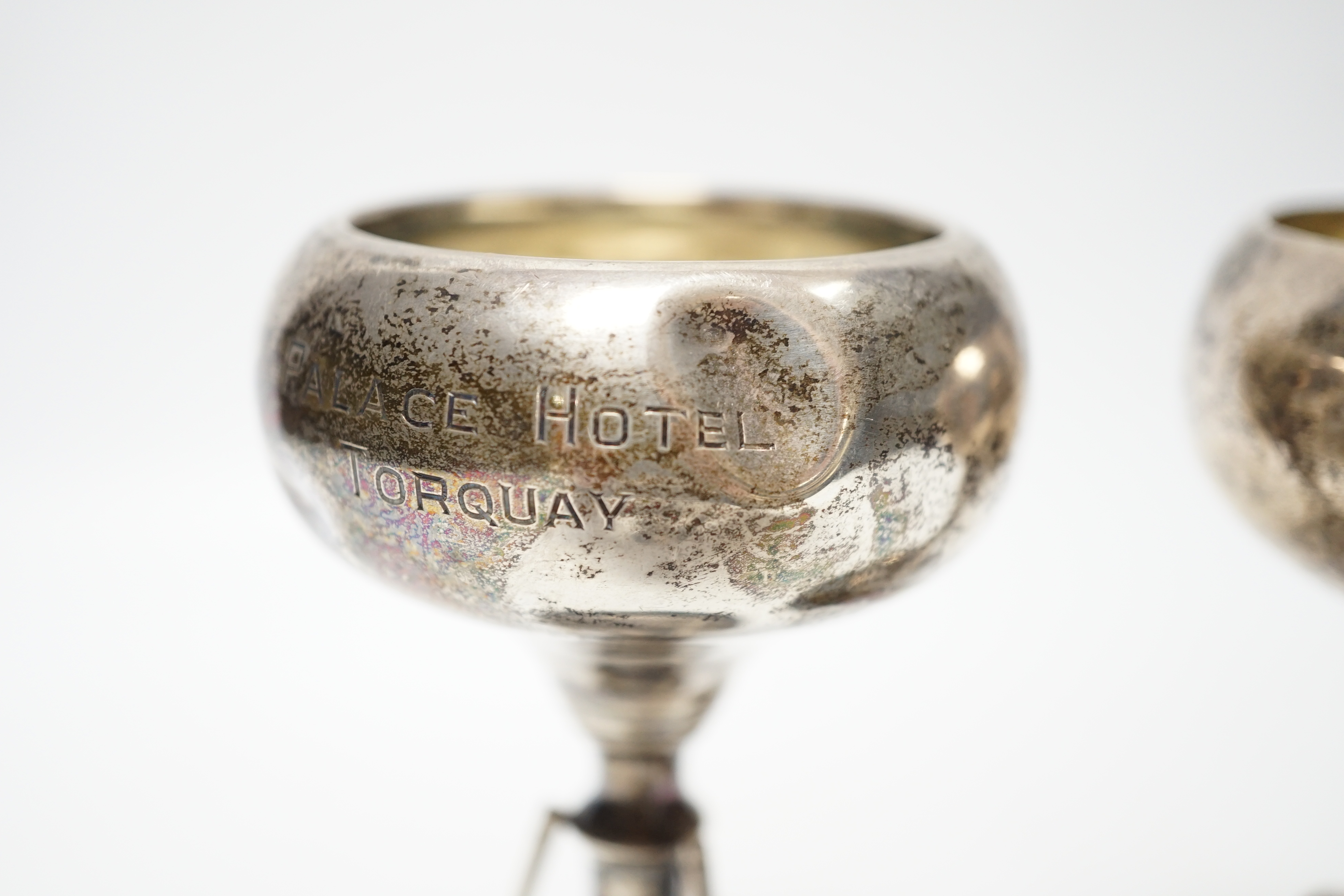 A set of three small George V silver tennis related trophy cups, with racket supports and engraved inscriptions, E & J Leek, 92mm, two with plinth bases.